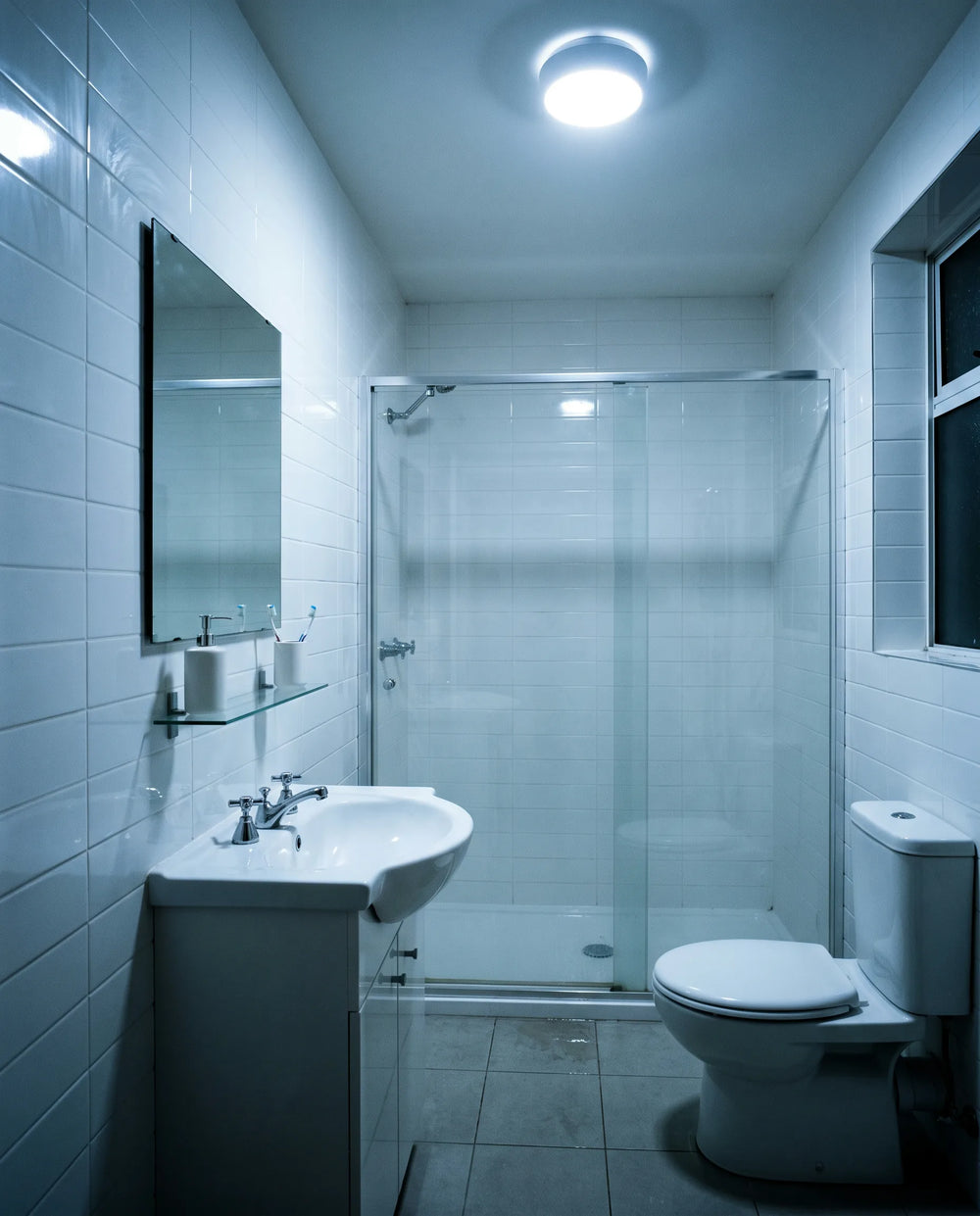 A bathroom at night under a harsh cool-white ceiling light